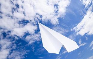 branco papel avião dentro uma azul céu com nuvens. a mensagem símbolo dentro a mensageiro foto