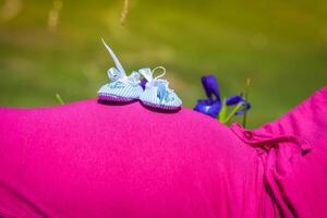 grávida mulher deitado em uma Relva com bebê sapatos em dela barriga foto