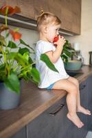 bebê menina Loiras comendo a maçã dentro a cozinha, conceito do saudável Comida para crianças foto