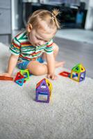 pequeno menina jogando colorida magnético plástico blocos kit às lar. a criança jogando educacional jogos. cedo infância desenvolvimento. foto