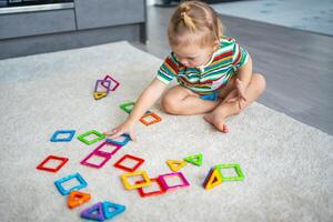 pequeno menina jogando colorida magnético plástico blocos kit às lar. a criança jogando educacional jogos. cedo infância desenvolvimento. foto