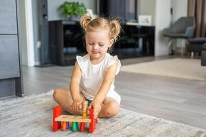 fofa caucasiano pequeno menina jogando em a chão às casa com eco de madeira brinquedos. montessori brinquedo. a criança jogando educacional jogos. foto