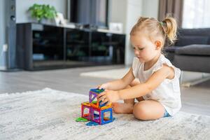 pequeno menina jogando colorida magnético plástico blocos kit às lar. a criança jogando educacional jogos. cedo infância desenvolvimento. foto