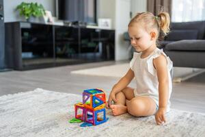 pequeno menina jogando colorida magnético plástico blocos kit às lar. a criança jogando educacional jogos. cedo infância desenvolvimento. foto