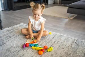 fofa pequeno criança pequena menina jogando às casa com eco de madeira brinquedos. feliz criança corte legumes e frutas com brinquedo faca. a criança jogando educacional jogos. foto