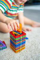 pequeno menina jogando colorida magnético plástico blocos kit às lar. a criança jogando educacional jogos. cedo infância desenvolvimento. foto