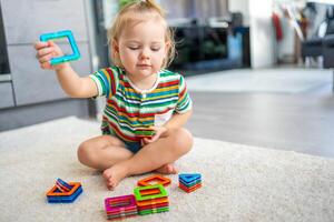 pequeno menina jogando colorida magnético plástico blocos kit às lar. a criança jogando educacional jogos. cedo infância desenvolvimento. foto