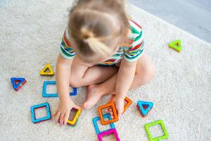 pequeno menina jogando colorida magnético plástico blocos kit às lar. a criança jogando educacional jogos. cedo infância desenvolvimento. foto