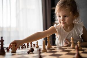pequeno menina jogando xadrez às a mesa dentro casa cozinha. a conceito cedo infância desenvolvimento e Educação. família lazer, comunicação e lazer. foto