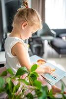 adorável criança pequena pequeno menina lendo livro às lar. felicidade criança lendo livro para pré escola apreciar com Aprendendo Educação de você mesmo. Educação conceito foto