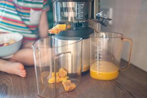 pequeno menina fazer fresco suco em a mesa dentro casa cozinha. foco em espremedor foto