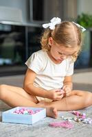 pequeno menina fazer de madeira miçangas pulseira às casa vivo sala. crianças criatividade e a desenvolvimento do bem motor Habilidades foto