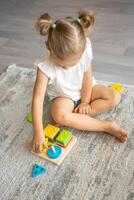 fofa caucasiano pequeno menina jogando em a chão às casa com eco de madeira brinquedos. a criança jogando educacional jogos. foto