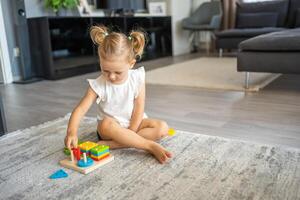 fofa caucasiano pequeno menina jogando em a chão às casa com eco de madeira brinquedos. montessori brinquedo. a criança jogando educacional jogos. foto