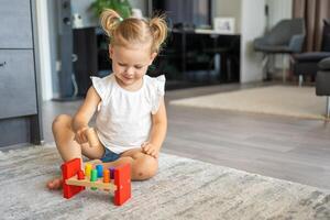 fofa caucasiano pequeno menina jogando em a chão às casa com eco de madeira brinquedos. montessori brinquedo. a criança jogando educacional jogos. foto