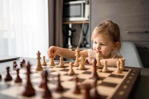 pequeno menina jogando xadrez às a mesa dentro casa cozinha. a conceito cedo infância desenvolvimento e Educação. família lazer, comunicação e lazer. foto