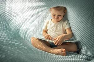 pequeno menina desfrutando do Reveja uma livro debaixo azul tricotado xadrez dentro ensolarado manhã foto