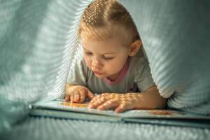 pequeno menina desfrutando do Reveja uma livro debaixo azul tricotado xadrez dentro ensolarado manhã foto