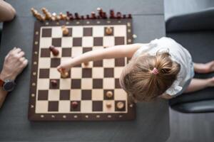 pequeno menina jogando xadrez com dela pai às a mesa dentro casa cozinha. a conceito cedo infância desenvolvimento e Educação. família lazer, comunicação e lazer. foto