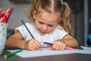 pequeno menina desenha com colori lápis dentro lar. foto