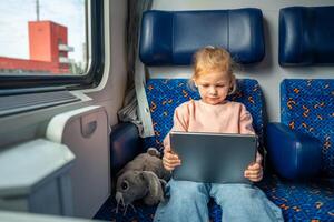 pequeno menina usando digital tábua durante viajando de estrada de ferro dentro Alemanha, Europa foto