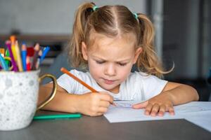 pequeno menina desenha com colori lápis dentro lar. foto