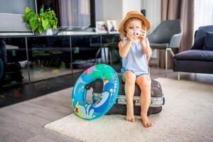 pequeno menina com mala de viagem Bagagem bagagem e inflável vida bóia jogando com brinquedo Câmera e pronto para ir para viajando em período de férias foto