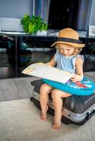 pequeno menina com mala de viagem Bagagem bagagem e inflável vida bóia lendo mapa e pronto para ir para viajando em período de férias foto