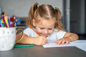 pequeno menina desenha com colori lápis dentro lar. foto