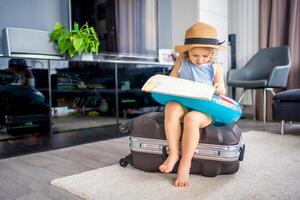 pequeno menina com mala de viagem Bagagem bagagem e inflável vida bóia lendo mapa e pronto para ir para viajando em período de férias foto