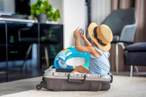 pequeno menina com mala de viagem Bagagem bagagem e inflável vida bóia jogando com brinquedo Câmera e pronto para ir para viajando em período de férias foto