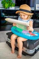pequeno menina com mala de viagem Bagagem bagagem e inflável vida bóia lendo mapa e pronto para ir para viajando em período de férias foto
