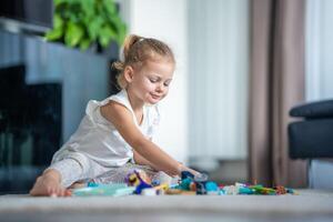 fofa pequeno menina tocam com pequeno construtor brinquedo em chão dentro lar, educacional jogo, gastos lazer Atividades Tempo conceito foto