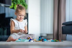 pequeno menina jogar com pequeno construtor brinquedo em chão dentro casa vivo sala, educacional jogo, gastos lazer Atividades Tempo conceito foto