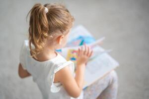 fofa pequeno menina é sentado e folheando através uma livro com fada contos foto