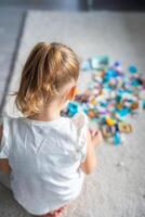 pequeno menina jogando com pequeno construtor brinquedo em chão dentro lar, Visão a partir de a voltar, educacional jogo, gastos lazer Atividades Tempo conceito foto