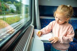 pequeno menina desenha com lápis em branco papel enquanto viajando de estrada de ferro dentro tcheco república, Europa foto