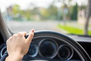 Visão do uma mulher mão em a direção roda do uma carro enquanto dirigindo dentro a cidade foto