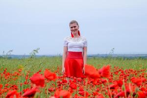 Loiras jovem mulher dentro vermelho saia e branco camisa, vermelho brincos é dentro a meio do uma papoula campo. foto