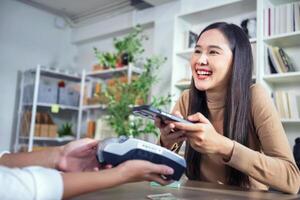 jovem ásia mulher sorridente e pagando com Smartphone dentro restaurante foto