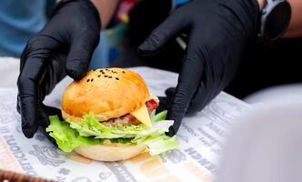 Hambuger mini, profissional mão chefe de cozinha segurando fresco delicioso e saboroso feito à mão hambúrguer, enfeitado com salada, tomates, e pepino dentro uma fechar-se tomada, velozes Comida para seu rápido estilo de vida foto