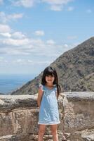 latina turista pequeno menina posando para uma foto com montanhas e nuvens fundo.