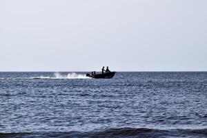 a barco corre de a mar. dentro a barco pessoas. marinha dentro a tarde. silhueta do uma motor barco e pessoas dentro isto contra a fundo do a mar distância foto