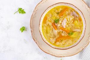 fresco frango sopa com legumes e estelino massa dentro uma tigela com cenoura e salsinha. topo visualizar, plano deitar foto