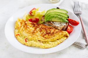 omelete com tomates e torrada com abacate em branco placa. fritada - italiano omelete. foto