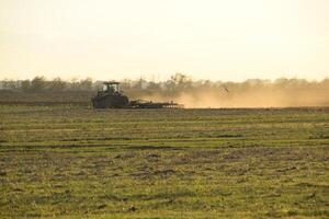 trator às pôr do sol arado arado uma campo. lavrando a solo dentro a outono depois de colheita. a fim do a estação foto