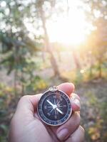 fechar acima do bússola dentro mulher mão com floresta dentro a pôr do sol Tempo Como fundo. a conceito do mundo turismo dia, procurando a certo instruções e viagem foto