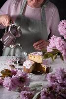 uma mulher derrama chá a partir de uma prata bule de chá, fundo do Rosa sakura flores, páscoa foto