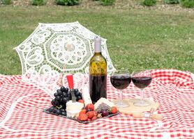 verão piquenique em uma verde gramado com vermelho vinho, queijo e fresco bagas, uvas foto