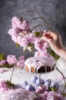 uma mulher decora uma caseiro Páscoa bolo com Rosa sakura flores, primavera Flor foto